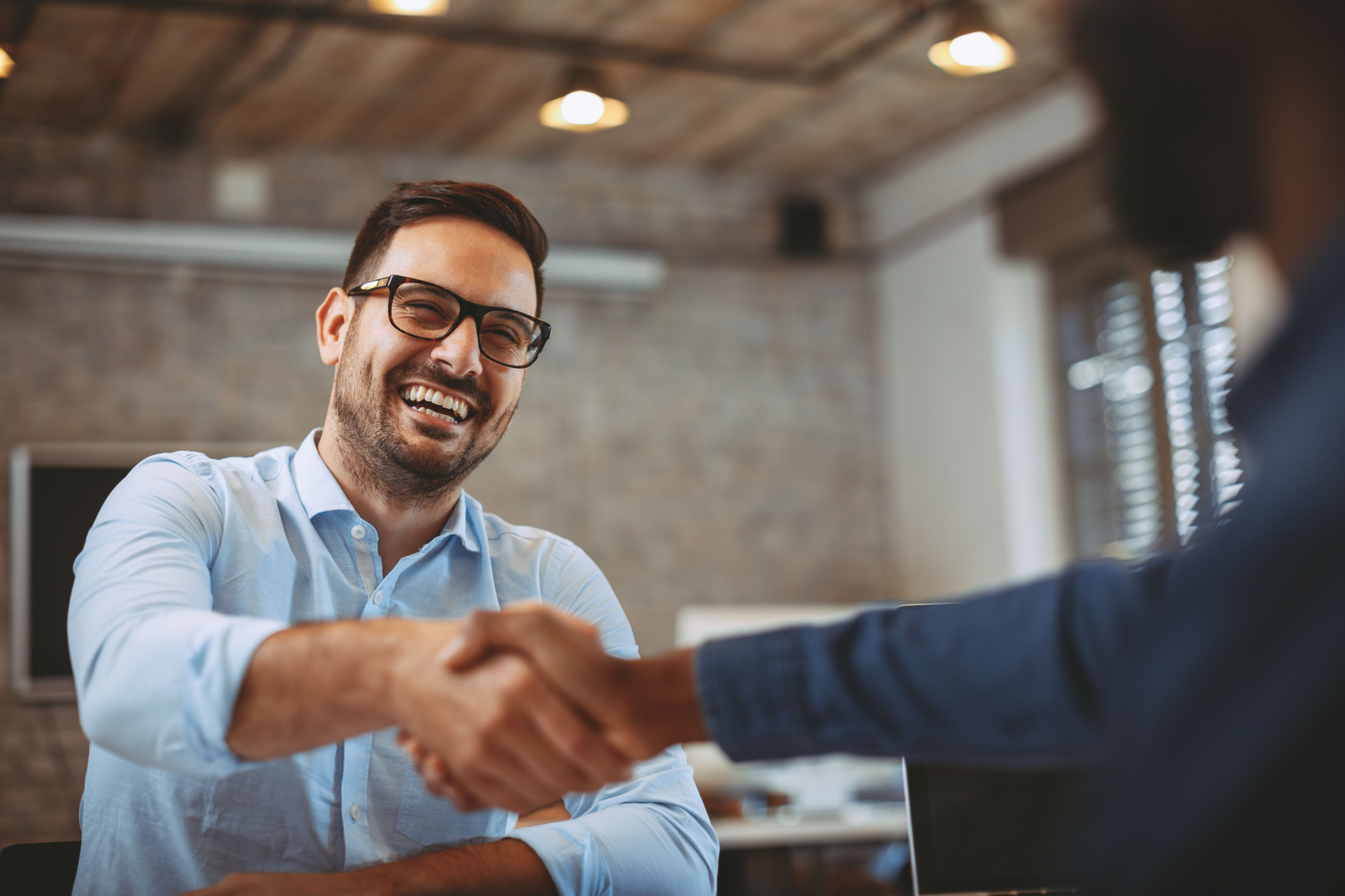 Real estate salesman happy as he closes a deal with a client, shaking hands with them.